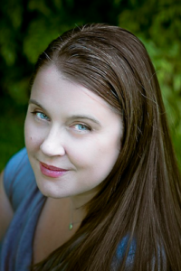 Instructor and cofounder Amanda Castleman, a smiling Caucasian woman with blue eyes and long brown hair. Pacific Northwest greenery is visible in the background. Photo by Valentina Vitols 