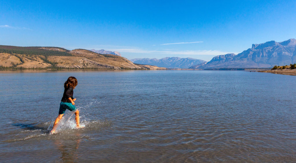 A young girl running in a lake with Canadian Rocky Mountains in the distance