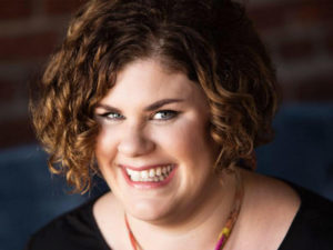 Amy Estes, a comedian and writer. Pic: a smiling woman with pale skin and dark brown curls