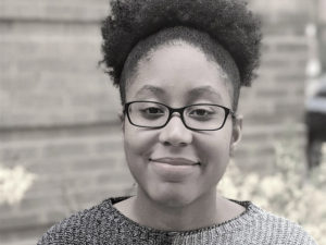 Writer Robin Mosley, an African-American woman with black glasses, a two-tone sweather and her Afro pulled back by a headband