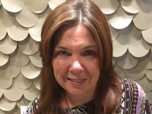 Journalist and book author Gillian Kedall, a white woman with brown, middle-parted, shoulder-length hair against a white "fish-scaled" background