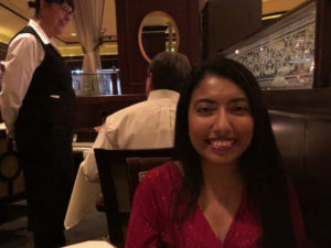 Journalist Sian Speakman sitting in the booth of an elegant restaurant. She is beaming and has long dark hair, which flows over ther V-neck, long-sleeved scarlet dress