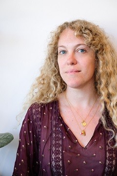 Writer Flora Tsapovsky from Tel Aviv, a white woman with long, curly blonde hair, a V-neck maroon blouse and a delicate necklace