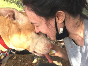 Writer Brijana Prooker wearing a black mask on her chin pressing her face to her pit bull's