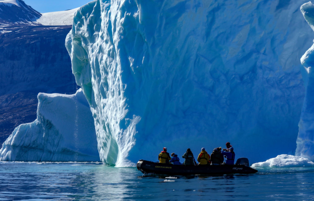 A Zodiac full of tourists photograph a giant blue iceberg in Greenland (image copyright Amanda Castleman)