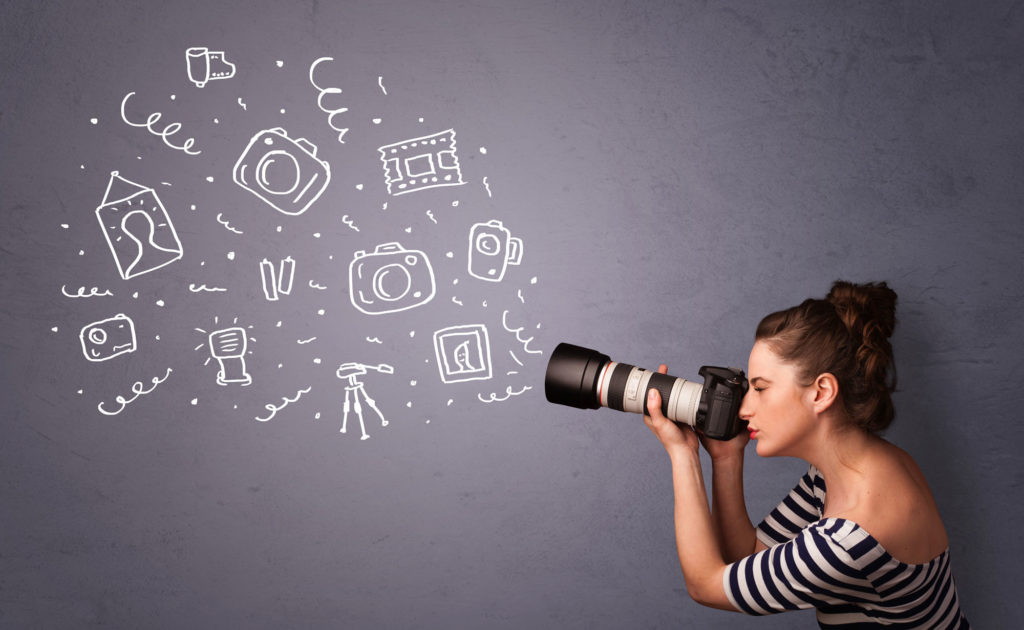 A young chic white-looking woman with a bun and b&w-striped shirt is photographing chalkboard images of photography with a Canon lens