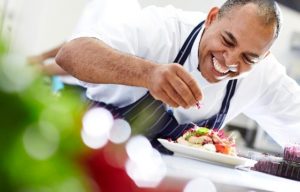 A smiling Black chef puts the finishing touches on a dish. Image sourced from Pixaby