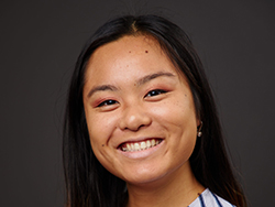 Portrait of a first-generation Chinese-American writer. She's photographed against a dark grey background with her long black hair down and parted on one side. She's smiling.