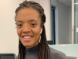 Portrait of the Black writer Monique M. Johnson. She's smiling and is wearing a grey turtleneck and her long box braids clipped back from her face.