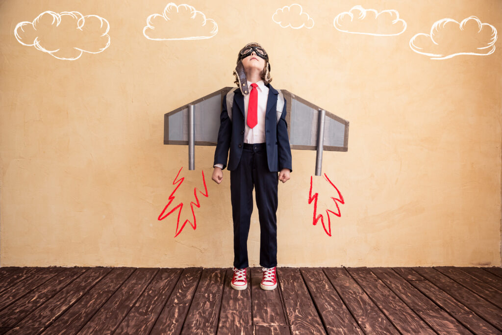 A stock illustration of a kid in a suit, red tie and red Chucks, standing against a pale orange wall with rocket-boosted wings and clouds painted on it